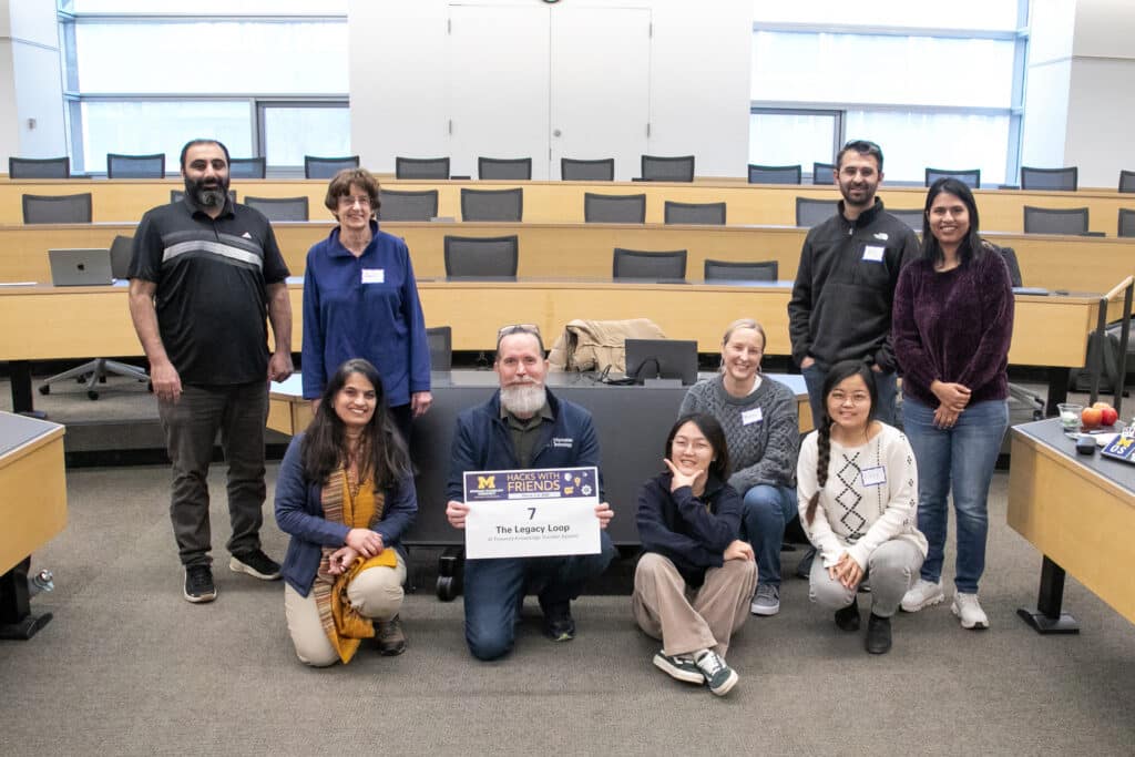 Don DuChateau, Sheetal Sonar, and their team hold a sign that says "The Legacy Loop: AI-Powered Legacy System"