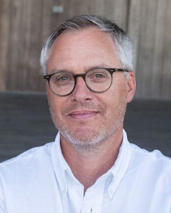 Gregg Latterman - Man with black-framed glasses and a white shirt in front of a neutral background