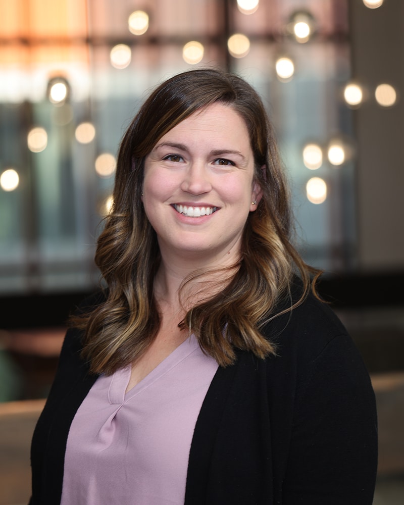 Megan Anda - woman with light brown hair wearing a pink shirt and black cardigan