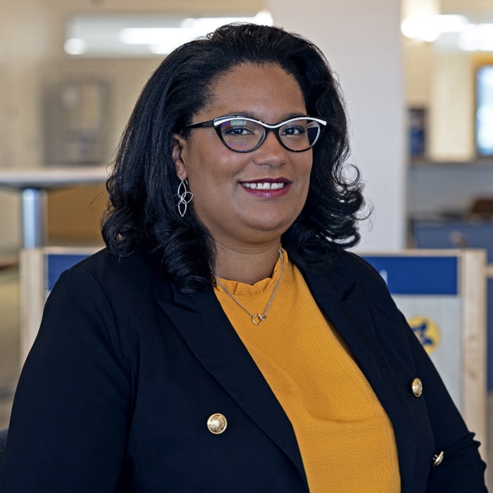 Deanna Arrieta-Murphy - woman with black hair and glasses wearing a maize shirt under a navy blue blazer
