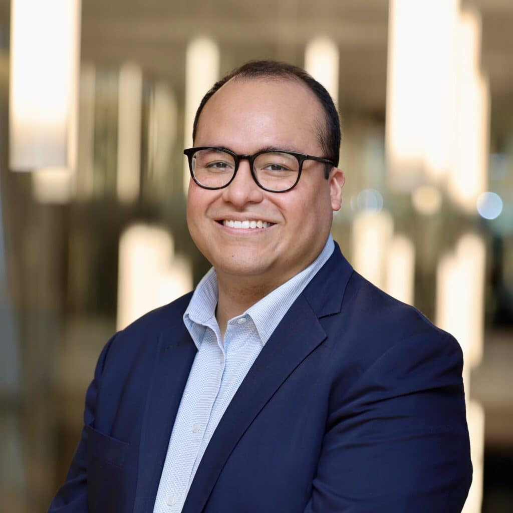 michael gaitan flores wearing glasses and a light blue shirt under a navy suit jacket