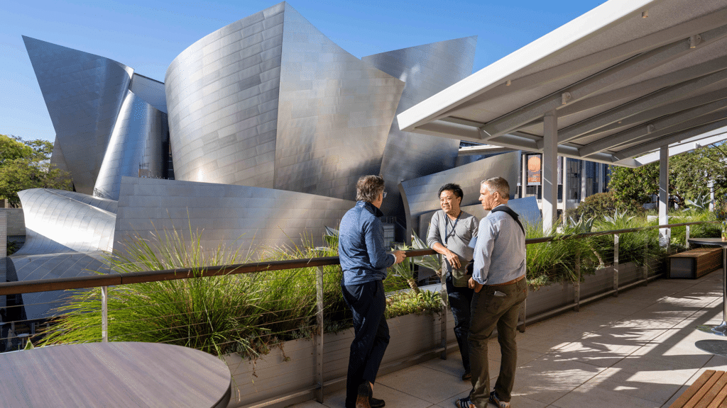 Three people speak on a balcony on the outside of the building.