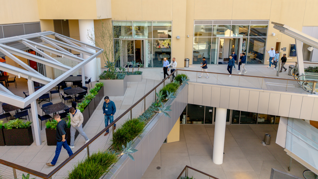 Several people walk on a balcony on the outside of the building.